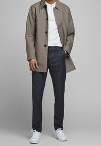 Ljusbrun houndstooth-jacka över en vit zip-up-tröja, i kombination med mörkgrå byxor och vita sneakers. Släta texturer och skräddarsydd passform.