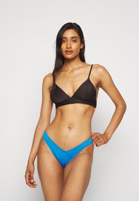 Top de biquíni preto com textura canelada e alças ajustáveis, combinado com um fundo de biquíni azul de cintura baixa. Textura suave e cores contrastantes.