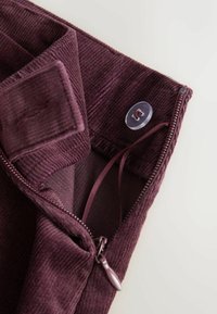 Burgundské kordové nohavice s viditeľným zipsom a zapínaním na gombík, s hladkým vnútorným podšívaním a tenkým stužkovým detailom vo vnútri.