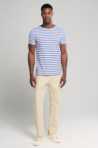 Stripet kortærmet t-shirt i hvid med blå vandrette striber; parret med beige lige bukser og hvide sneakers.