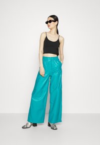 Calças largas turquesa em material brilhante, combinadas com um top cropped preto. A modelo usa óculos de sol pretos e botas pretas e brancas com padrão.