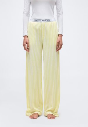 Personne portant un pantalon ample à rayures verticales jaunes et blanches avec une taille élastique Polo Ralph Lauren et un haut blanc ajusté à manches longues.