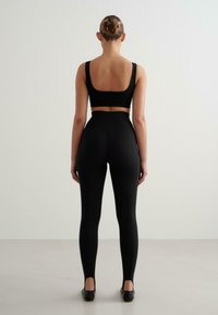 Svart matchande sport-bh och högmidjade leggings, tillverkade av ett slätt material. Bh:n har en skuren rygg och leggingsen har öppningar vid anklarna.