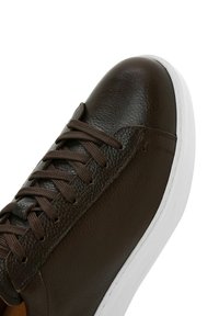 Brown leather sneaker with a smooth texture, round toe, and brown laces. Features a white rubber sole and subtle stitching details.