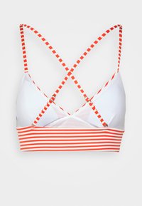 Bralette com riscas brancas e vermelhas, apresentando alças cruzadas, reguladores ajustáveis e uma textura suave nos copos e na banda.
