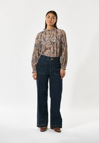Blusa floreale a maniche lunghe con scollo arricciato, abbinata a pantaloni flared in denim scuro a vita alta. Calzature marroni completano il look.