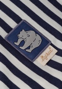 Marineblau- und weiß gestrefter Stoff mit einem strukturierten Bärenpatch in Blau und Grau. Enthält ein kleines Etikett mit "sigikid" in einem sanften Beige.