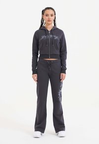 Zwarte cropped hoodie met zilveren tekst, voorzakken en rits; bijpassende zwarte sweatpants met een zijontwerp. Katoenmengsel.