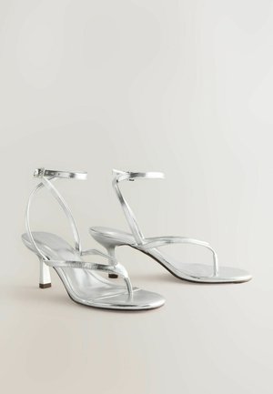 Des sandales à talons métalliques argentées présentent un design minimaliste avec des fines lanières et un talon block effilé. Texture lisse, style ouvert à l'avant.