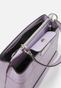 Borsa a tracolla lilla con motivo testurizzato del logo, finiture in argento, scompartimento con cerniera e tracolla rimovibile su uno sfondo bianco.