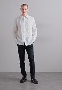 Hvid linnedskjorte, sorte slim-fit bukser og sorte sandaler. Skjorten har en knaplukning med krave og lange ærmer.