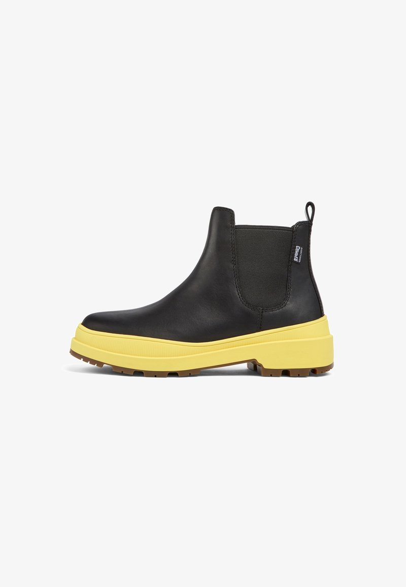Botte Chelsea en cuir noir avec semelle épaisse jaune, panneau latéral élastique, languette de traction et étiquette de marque à l'arrière.