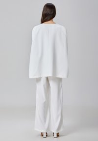 Haut blanc de style cape avec un décolleté arrondi, associé à un pantalon blanc à jambes larges. Tissu lisse, design minimaliste, lignes épurées.