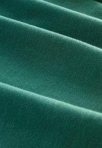 Türkise Stoff mit einer weichen, strukturierten Oberfläche, die subtile Fältchen und unterschiedliche Grüntöne aufweist und sich für verschiedene textile Anwendungen eignet.