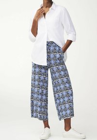 Chemise blanche à boutons, pantalon large à motifs bleus, design floral texturé, associé à des baskets blanches.