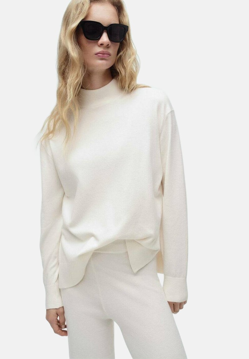 Crème-kleurig longsleeve shirt met hoge hals en een relaxte pasvorm, gecombineerd met bijpassende strakke broek. Soepele brei textuur, minimalistisch design.