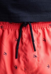 Korallfarbene Badeshorts mit kleinen dunkelblauen Hummer-Prints, elastischem Bund mit verstellbarem schwarzem Kordelzug und Metallenden. Glatte Textur.