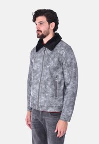Giacca in ecopelle grigia con colletto in shearling nero, tasca con zip, finitura testurizzata e chiusura frontale con zip.
