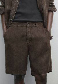 Bruna linnshorts med flat front, sidofickor och knappstängning. Slät textur med subtil lyster. Stylar med en mörk linne.