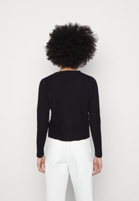 Suéter negro de canalé con cuello redondo, forma ajustada y mangas largas, que presenta un diseño recortado y una textura sutil.