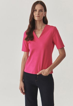 Top rosa a maniche corte con scollatura a V, realizzato in un tessuto morbido. Abbinato a jeans blu scuro con uno stile minimalista.