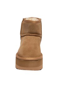 Stivaletto alla caviglia in suede tan con punta arrotondata, interno morbido e suola in gomma piatta. Presenta dettagli cuciti e un gambale basso.