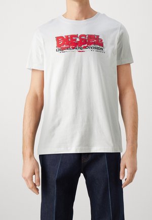 Bílý bavlněný tričko s opotřebovaným červeným a černým logem "DIESEL" a textem "DENIM DIVISION". Krátké rukávy a kulatý výstřih.