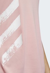 Rosa sporttröja i strukturerat material. Har tre sneda vita ränder med ett slitet mönster längs den vänstra sidan.