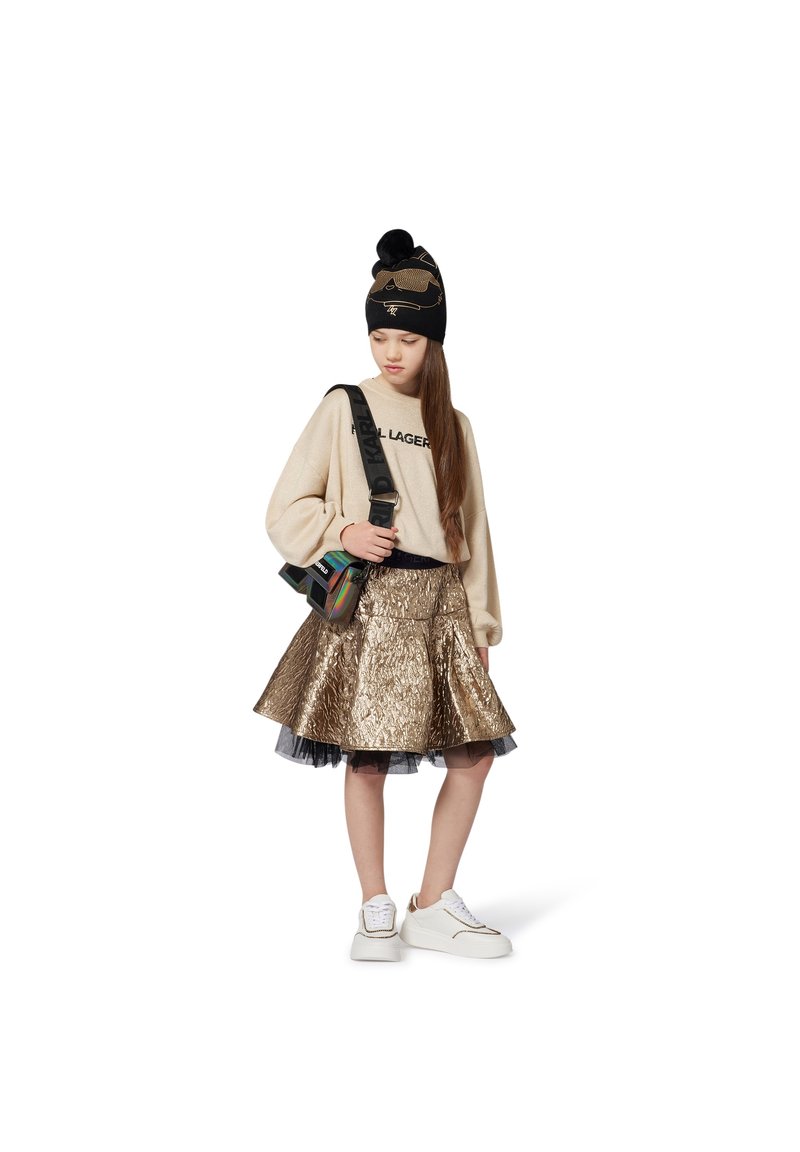 Bež pulover s črnim logotipom, kovinsko zlatorumen flare krilo s črnim tila podlog, črna kapa s zlatimi poudarki, bele superge.