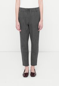Pantalones grises, ceñidos, confeccionados con una tela texturizada, con una cinturilla elástica y cordón de ajuste. Llevados con zapatos de terciopelo burdeos tipo slip-on.