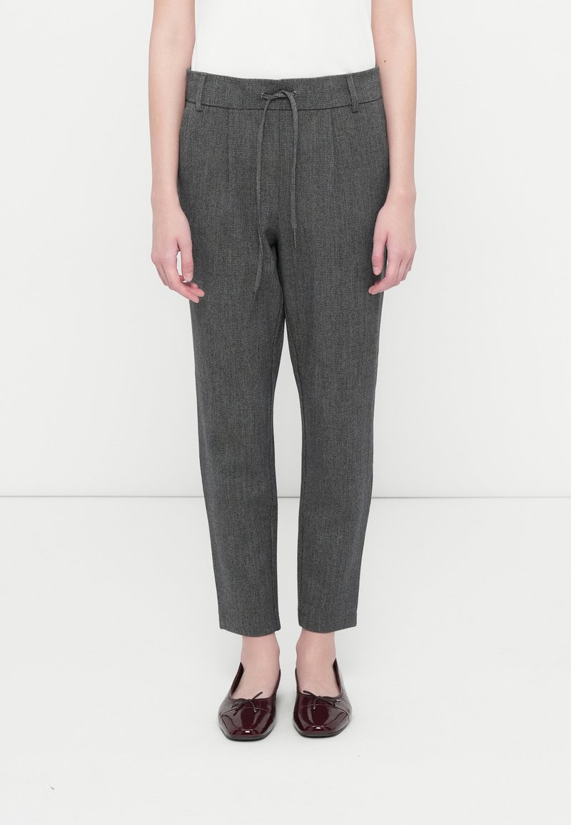 Pantalones grises, ceñidos, confeccionados con una tela texturizada, con una cinturilla elástica y cordón de ajuste. Llevados con zapatos de terciopelo burdeos tipo slip-on.