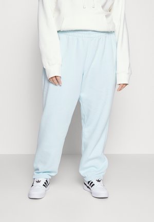 Person wearing light blue sweatpants, white hoodie, and white sneakers with black stripes, standing against a plain background.