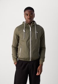 Olivgrüne Zip-Jacke mit Kapuze, weißen Reißverschlussdetails, verstellbaren Kordeln und zwei seitlichen Reißverschlusstaschen. Glattes, leichtes Material.