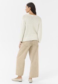 Pull en tricot beige clair avec des manches larges et des poignets côtelés, associé à un pantalon large beige et des ballerines beiges. Texture lisse, design minimaliste.