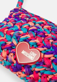 Vævet håndtaske i multicolor stof med pink, blå, orange og lilla teksturer. Inkluderer et rødt hjerteformet logo med "LOVE MOSCHINO."