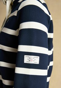 Marineblaue und weiße, horizontal gestreifte Langarmshirt mit einem rechteckigen Etikett am Ärmel mit der Aufschrift "Joules Clothing" und "Mariners Grade".