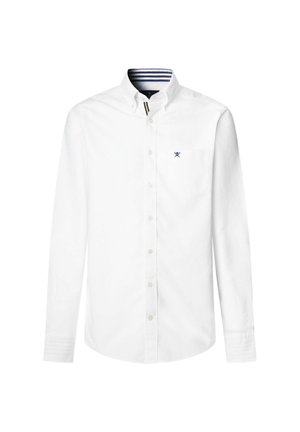 Camisa blanca de manga larga con botones y cuello, que presenta un pequeño bolsillo en el pecho y un detalle a rayas azul marino en el interior del cuello. Fabricada en tela de algodón.