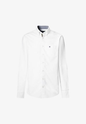 Biała, długosleeva koszula zapinana na guziki z kołnierzykiem, z małą kieszonką na piersi i granatowym paskowanym wykończeniem wewnątrz kołnierza. Wykonana z bawełnianej tkaniny.