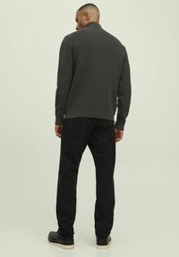Dunkelgrauer gerippter Pullover mit hohem Kragen, kombiniert mit schwarzen Hosen und schwarzen Schuhen, mit einer glatten Textur und tailliertem Schnitt.