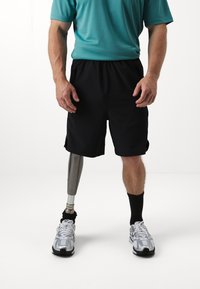 Pantalones cortos atléticos negros, camiseta de manga corta color turquesa, pierna prostética plateada, zapatillas de correr blancas y negras, calcetines negros hasta el tobillo.