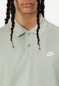 Light green polo shirt, short sleeves, with a collar and two buttons. Features a small white Nike logo on the chest. Textured fabric.