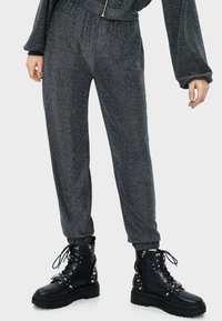 Szare metaliczne dresy z elastycznym pasem i ściągaczami na kostkach, w połączeniu z czarnymi skórzanymi butami wojskowymi z nitowanymi akcentami.