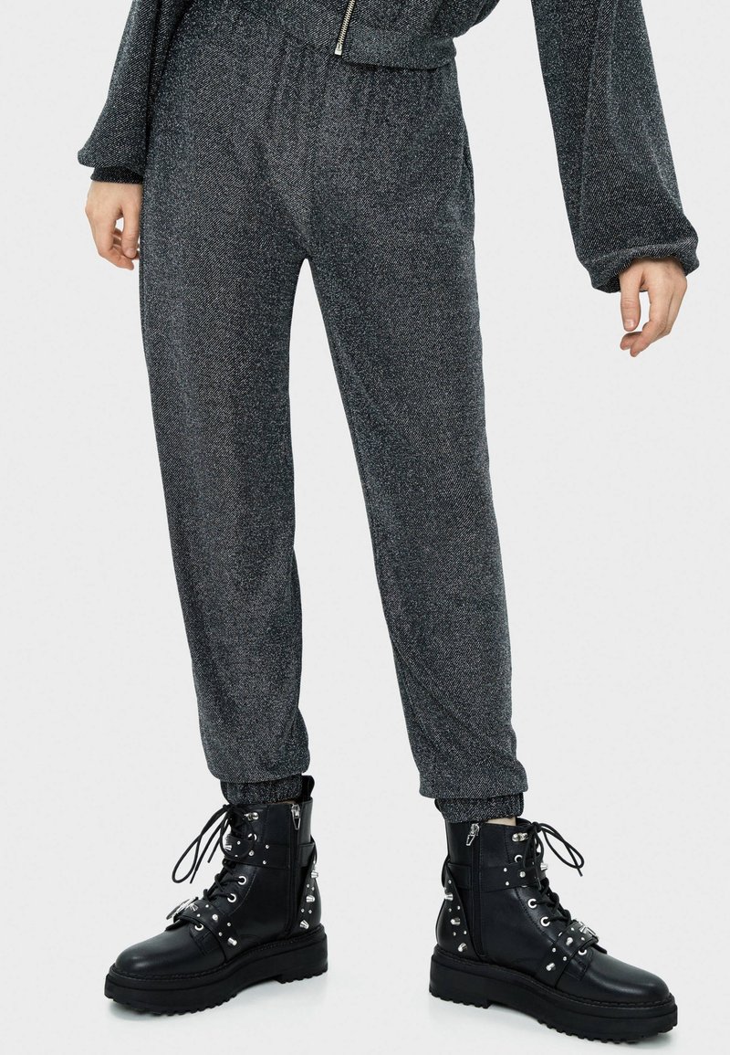 Szare metaliczne dresy z elastycznym pasem i ściągaczami na kostkach, w połączeniu z czarnymi skórzanymi butami wojskowymi z nitowanymi akcentami.