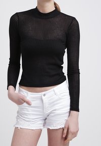 Top negro de manga larga con textura acanalada y cuello alto, combinado con pantalones cortos blancos con detalles de encaje y bordes deshilachados.