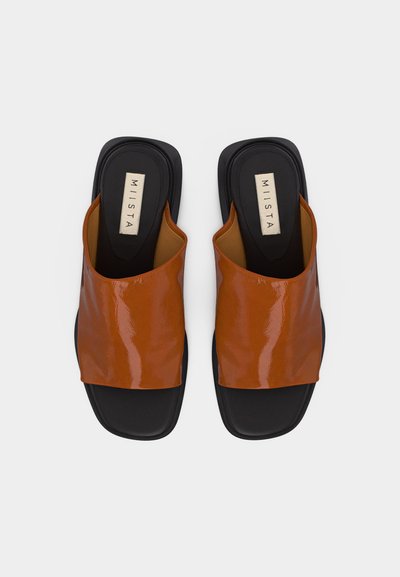 Ζευγάρι μαύρων σανδαλιών τύπου slide με γυαλιστερές καφέ φαρδιές λουρίδες και τετράγωνα δάχτυλα, με ετικέτα "MIISTA" στις εσωτερικές σόλες.
