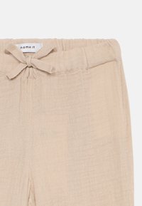 Beige vevde bukser med et mykt, strukturert stoff. Har en elastisk midje med en dekorativ sløyfe og en avslappet passform.
