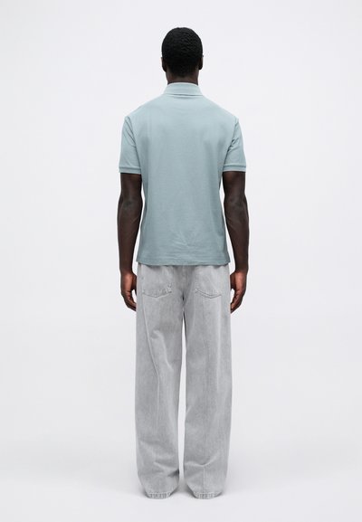 Ανοιχτό μπλε πόλο μπλουζάκι με κοντά μανίκια, συνδυασμένο με χαλαρά, ανοιχτού γκρί τζιν παντελόνια. Το υλικό φαίνετ�αι μαλακό και χαλαρό.