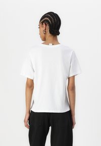 Hvid kortærmet t-shirt med rund hals, sideslidser i kanten og et lille mærke bag på halsen.