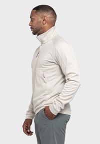 Halbzip-Fleece-Pullover in Hellbeige, mit hohem Kragen, langen Ärmeln und einer Brusttasche mit Reißverschluss. Glatte Textur.