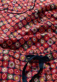 Mintás pamut pizsama szett, piros alapon, színes gyémánt és virágmintákkal; tartalmaz egy sötétkék, húzózsinóros derékrészt és gombokat.